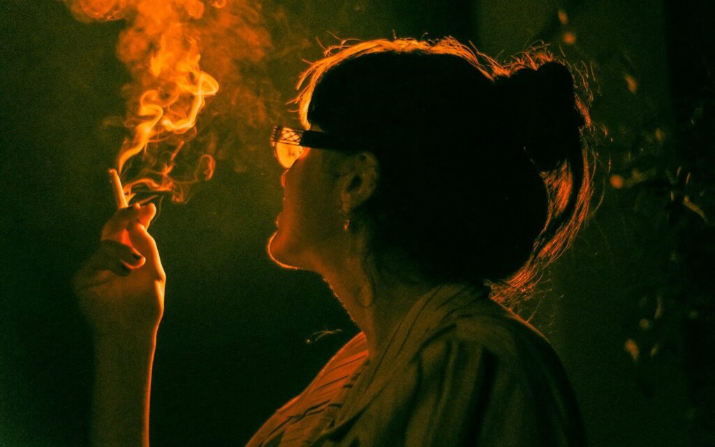 A woman smokes a cigarette, backlit by orange light